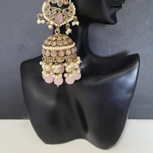 May include: Gold-toned chandelier earrings with a floral design and pink accents. The earrings feature a flower-shaped top, a domed center, and dangling pink beads and white pearls. The earrings are displayed on a black mannequin head.
