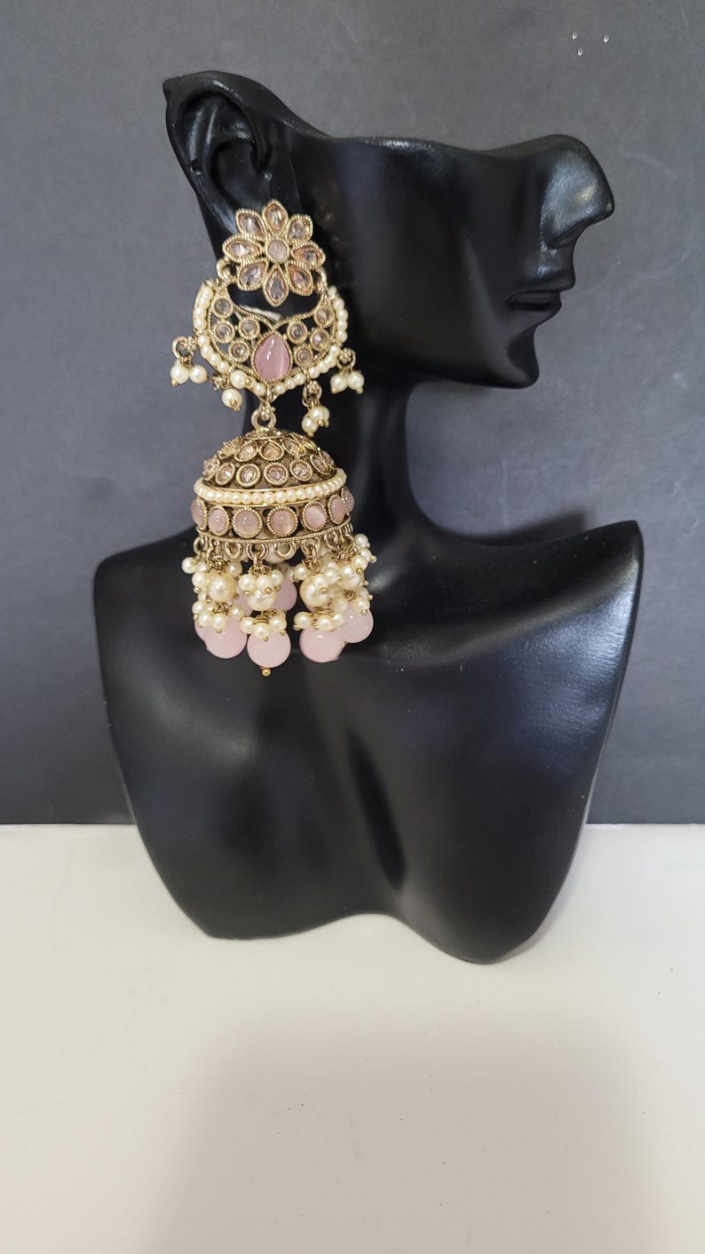 May include: Gold-toned chandelier earrings with a floral design and pink accents. The earrings feature a flower-shaped top, a domed center, and dangling pink beads and white pearls. The earrings are displayed on a black mannequin head.