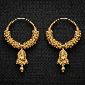 May include: A pair of gold-coloured hoop earrings. The hoops are decorated with small, round beads and have a dangling bell-shaped charm with intricate detailing. The earrings are set against a dark, textured background.