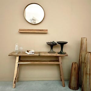 Könnte beinhalten: Ein Konsolentisch aus Holz mit einem Regal, zwei dekorativen Schalen und zwei hohen, zylindrischen Vasen. Der Tisch hat eine natürliche Holzoptik und die Vasen sind aus geflochtenem Bambus.
