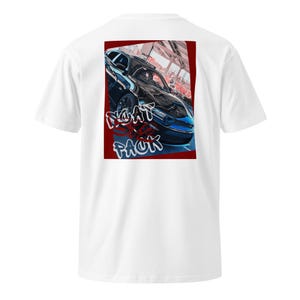 May include: White t-shirt featuring a graphic of a blue car with the text "MEAT PACK" in a stylized font. The graphic is set against a red background. The shirt is a classic crew neck style.