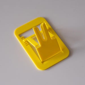 May include: A bright yellow plastic phone stand with a rectangular base and a built-in support. The stand has a slot to hold a phone upright. The design is simple and functional, suitable for desks or tables.