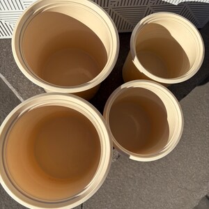 May include: Four cream-colored ceramic containers with rounded edges and smooth surfaces. The containers are arranged in a pyramid shape, with the largest container at the bottom and the smallest container at the top.