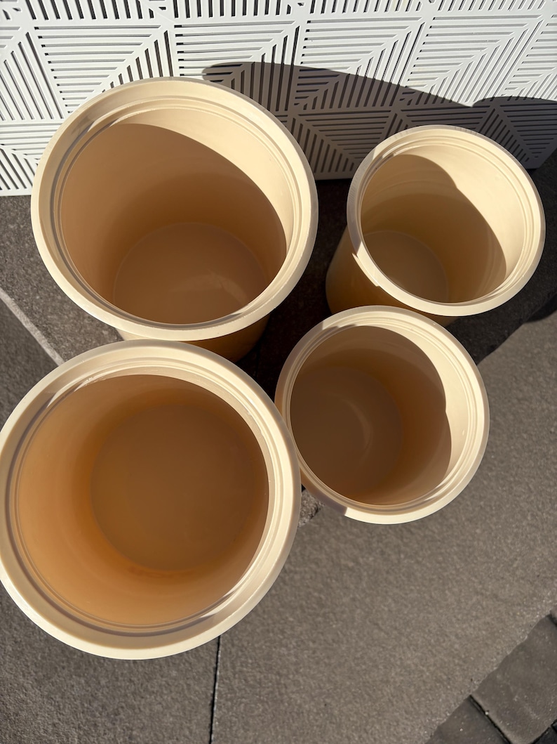 May include: Four cream-colored ceramic containers with rounded edges and smooth surfaces. The containers are arranged in a pyramid shape, with the largest container at the bottom and the smallest container at the top.