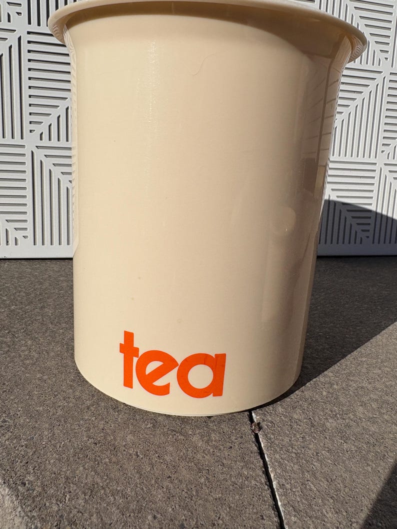 May include: A white ceramic tea canister with the word "tea" printed in orange.