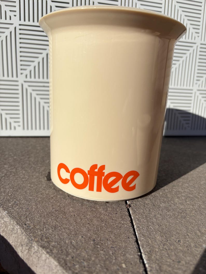 May include: A beige ceramic coffee canister with the word "coffee" printed in orange on the front.