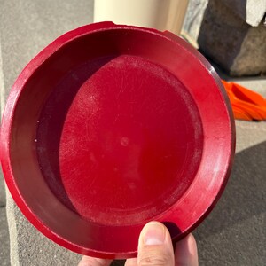 May include: A red plastic lid for a container. The lid is round and has a smooth surface.