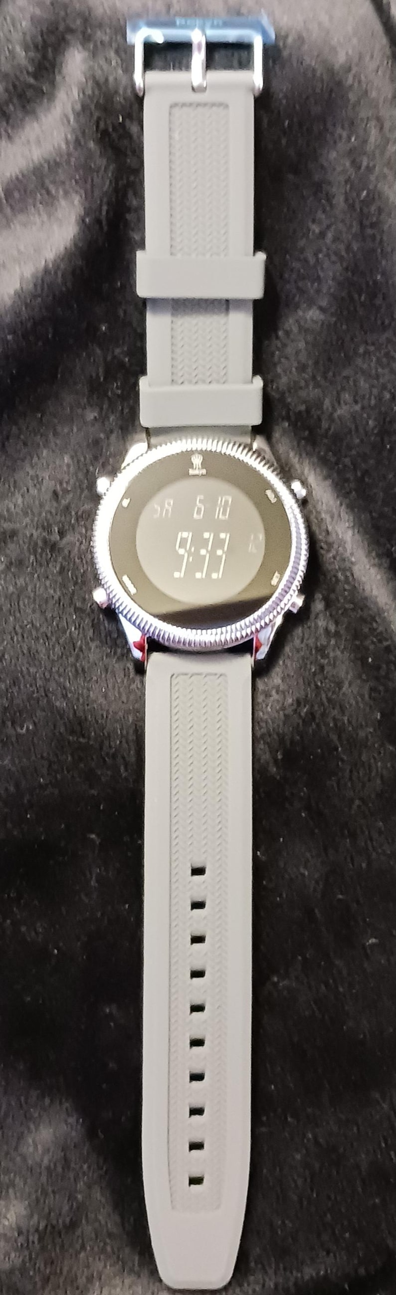 May include: A digital wristwatch with a gray silicone band. The watch face displays the date as 'SA 6 10' and the time as '9:33'. The watch has a silver-colored bezel and a blue clasp.