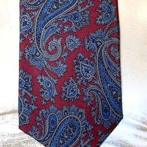 Puede incluir: Corbata burdeos con un estampado de cachemir repetido en tonos azules y grises. La tela es lisa. Adecuada para ocasiones formales, la corbata mide unos 147 cm de largo.