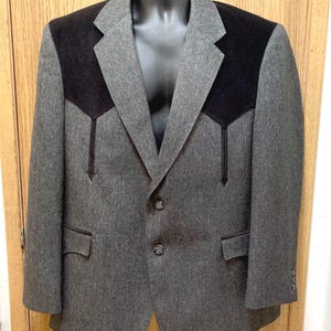 May include: A gray blazer with black shoulder accents and decorative stitching. The blazer has two buttons and two front pockets. The jacket is displayed on a black mannequin.