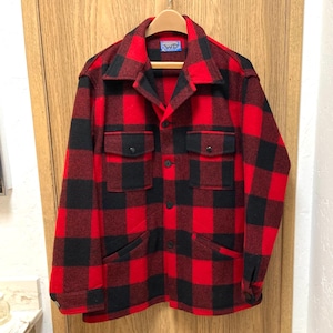 May include: A long-sleeve button-up jacket featuring a bold red and black buffalo plaid pattern. The garment includes a pointed collar, two chest pockets with buttoned flaps, two lower side pockets, and a blue label at the inner neckline.