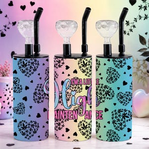 May include: Three cylindrical tumblers with black lids, clear glass bowls, and black straws. The tumblers feature a pattern of black hearts filled with leaf shapes. The center tumbler displays the text "I'M A LITTLE HIGH MAINTENANCE" in pink and blue.