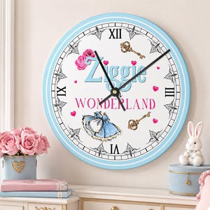May include: A round wall clock with a light blue frame, white face, and black Roman numerals. The center features the text Ziggie in WONDERLAND in blue and pink, surrounded by illustrations of pink roses, gold keys, hearts, and a blue dress.