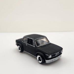 May include: A matte black miniature car with silver trim and wheels. The toy car has a classic coupe design, with a detailed front grille and headlights. The car is set against a plain white background.