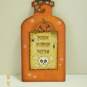 May include: Orange pumpkin shaped bottle with a skull and crossbones and the text "Poison Pumpkin Potion" on a label. The bottle has a cork stopper with a white cross on top.