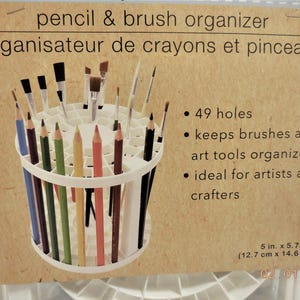 Op de afbeelding: Witte potlood- en penseelorganizer met 49 gaten, met diverse kleurpotloden en penselen. De tekst op de verpakking luidt "pencil & brush organizer" en "organisateur de crayons et pinceaux". Afmetingen: 12,7 cm x 14,6 cm.