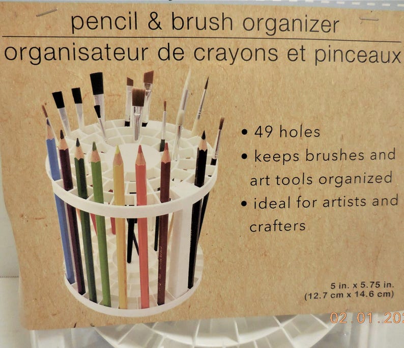 Op de afbeelding: Witte potlood- en penseelorganizer met 49 gaten, met diverse kleurpotloden en penselen. De tekst op de verpakking luidt "pencil & brush organizer" en "organisateur de crayons et pinceaux". Afmetingen: 12,7 cm x 14,6 cm.