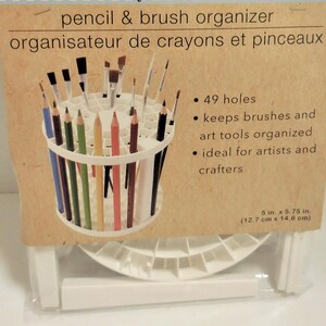 Op de afbeelding: Witte potlood- en penseelorganizer met een cilindrisch ontwerp, met diverse kleurpotloden en penselen. De verpakking leest "pencil & brush organizer" en bevat de afmetingen: 12,7 cm x 14,6 cm.