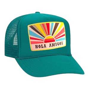 Puede incluir: Una gorra de camionero de color turquesa con un gráfico de amanecer colorido y el texto "Hola Amigos" en la parte delantera.