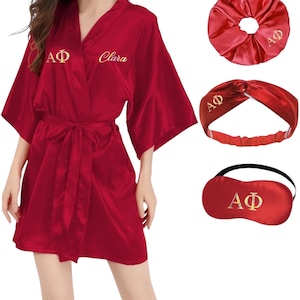 Può includere: Un set di accappatoio, scrunchie, fascia e mascherina per gli occhi in raso bordeaux. L'accappatoio ha una cintura annodata e lettere dorate ricamate. Lo scrunchie, la fascia e la mascherina per gli occhi hanno anche ricami dorati. L'accappatoio ha il nome "Clara".