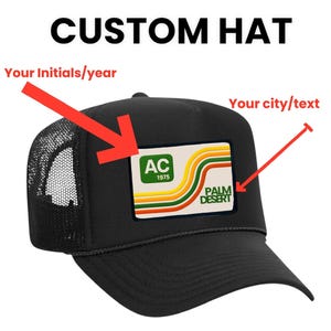 Peut inclure: Casquette de camionneur noire avec un dos en filet et une visière incurvée. L'écusson avant présente un design rétro avec le texte "PALM DESERT" et les initiales "AC 1975". Le texte "CUSTOM HAT" est au-dessus.