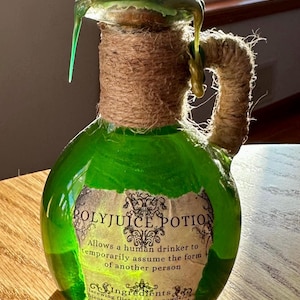 Puede incluir: Una botella de vidrio verde con un tapón de corcho y un asa de cuerda marrón. La botella está llena de un líquido verde y tiene una etiqueta que dice "Polyjuice Potion" y describe los efectos de la poción. La etiqueta también enumera los ingredientes de la poción.