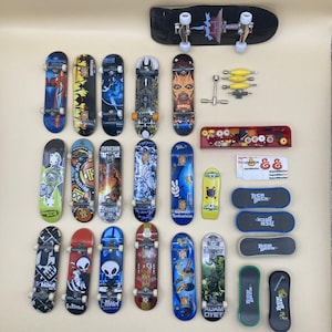 May include: A collection of finger skateboards featuring various graphic designs, including brands like Blind and Tech Deck. The set includes multiple complete boards with wheels and trucks, spare yellow wheels, a metal tool, a red storage tray, and stickers.