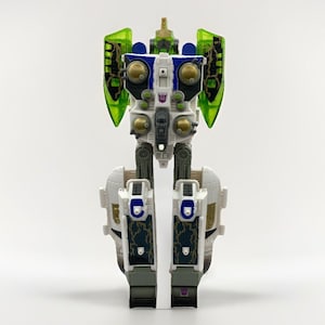 Puede incluir: Una figura de acción de robot con un esquema de color blanco, azul y gris con accesorios translúcidos verdes en forma de alas. El pecho muestra una insignia Decepticon morada, mientras que las piernas y el torso incorporan detalles dorados.