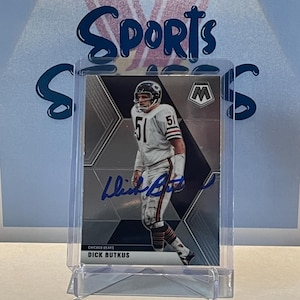 Puede incluir: Una tarjeta de intercambio plateada y negra con un jugador de fútbol americano que lleva una camiseta blanca con el número 51. El jugador es Dick Butkus, un ex linebacker de los Chicago Bears. La tarjeta tiene una firma azul y el texto "Chicago Bears" y "Dick Butkus".