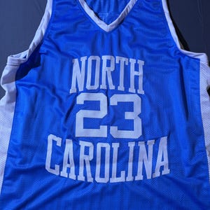 May include: A Carolina blue basketball vest with white trim and a V-neck. The vest features the words "NORTH CAROLINA" in white block letters, with the number "23" in the centre.