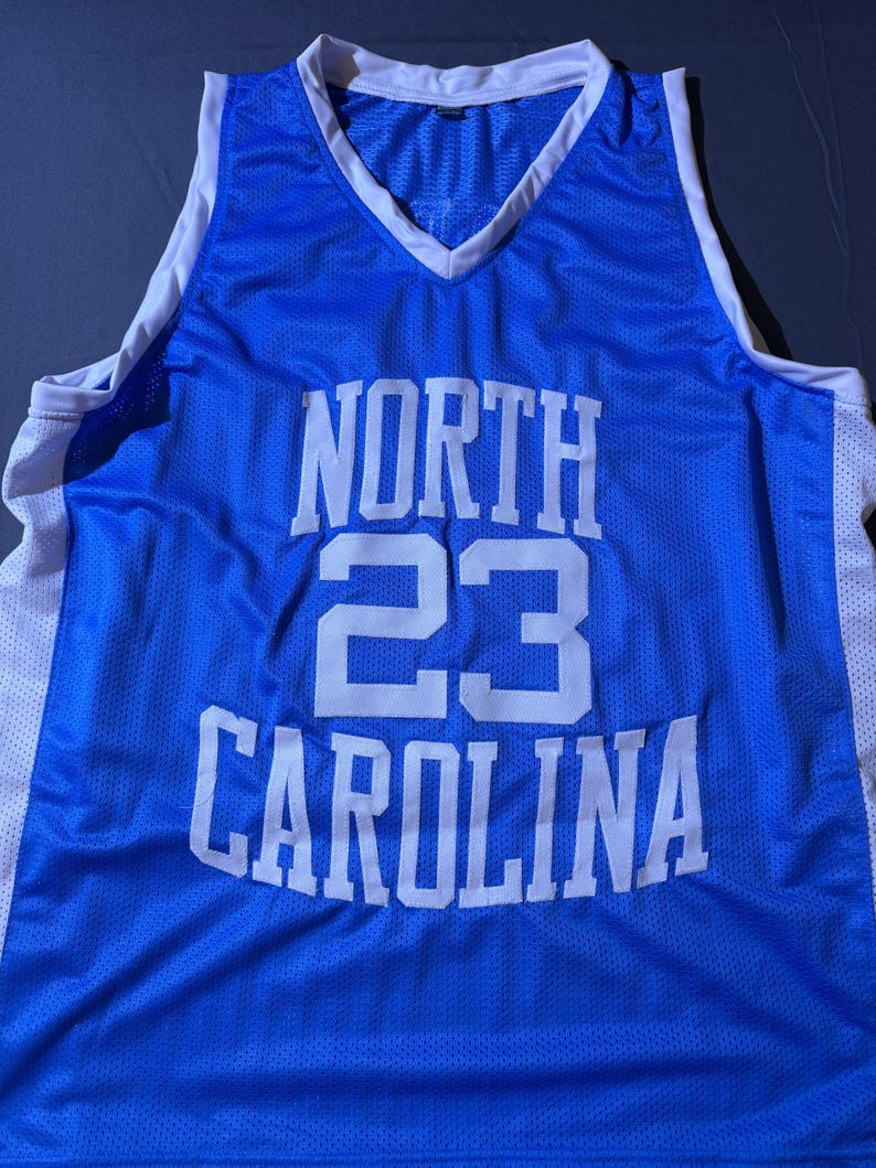 May include: A Carolina blue basketball vest with white trim and a V-neck. The vest features the words "NORTH CAROLINA" in white block letters, with the number "23" in the centre.