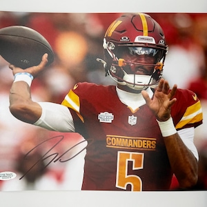 May include: A signed photograph of a football player in a burgundy and gold uniform, throwing a football. The player wears a burgundy helmet with a gold stripe and the number 5 on the jersey. The word "COMMANDERS" is visible on the jersey.