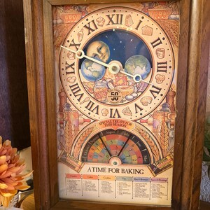 May include: A rectangular wooden wall clock featuring a decorative face with Roman numerals, a central illustration of the moon and earth, and a 50th anniversary Toll House cookies logo. The lower section displays a calendar and baking guide.