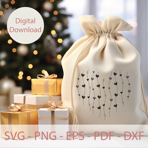 Op de afbeelding: Een witte stoffen cadeauzak met een zwart-wit ontwerp van harten op wijnstokken. De zak staat op een tafel met ingepakte cadeaus op de achtergrond. De tekst "SVG - PNG - EPS - PDF - DXF" staat onderaan de afbeelding.