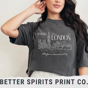 May include: A dark grey t-shirt with a white graphic of the London skyline, including Big Ben, and the text "SO LONG, APRIL 19 TTPD LONDON all's fair in love and poetry".