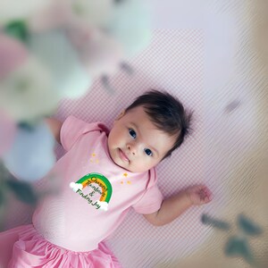 May include: A pink baby onesie with a green and yellow rainbow graphic and the text "Chasing Rainbows & Finding Joy".