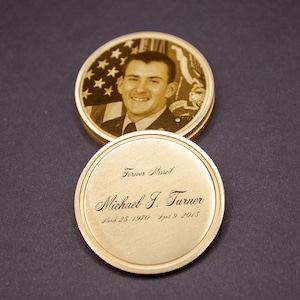 May include: A gold-colored commemorative coin with a portrait of a man in uniform and an American flag. The coin is engraved with the words "Forever Missed" and the name "Michael J. Turner" along with his birth and death dates.