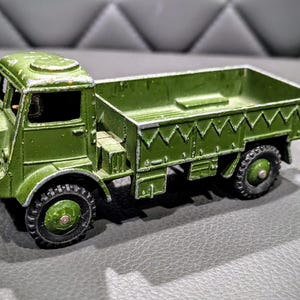 Puede incluir: Un cami&oacute;n de juguete verde con una plataforma y una cabina. El cami&oacute;n tiene un techo blanco y un volante negro. El cami&oacute;n est&aacute; hecho de metal y tiene un acabado de pintura desgastado.