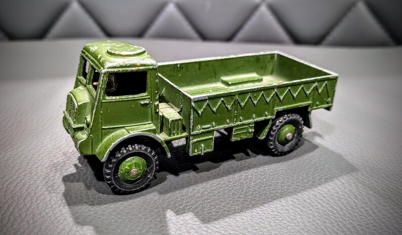 Puede incluir: Un cami&oacute;n de juguete verde con una plataforma y una cabina. El cami&oacute;n tiene un techo blanco y un volante negro. El cami&oacute;n est&aacute; hecho de metal y tiene un acabado de pintura desgastado.