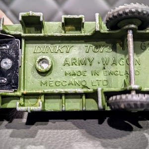 Puede incluir: Un carro de juguete verde del ej&eacute;rcito con ruedas negras y un eje de metal. La parte inferior del carro tiene el texto "Dinky Toys Army Wagon Made in England Meccano Ltd 625" impreso en &eacute;l.