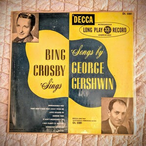Peut inclure: Une pochette de disque vinyle jaune et noire avec une photo de Bing Crosby et George Gershwin. Le titre est "Bing Crosby Sings Songs by George Gershwin". Le label du disque est Decca et le numéro du disque est DL 5081.
