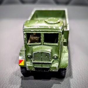 Puede incluir: Un cami&oacute;n de juguete verde con un conductor en la cabina. El cami&oacute;n tiene una plataforma y una marca amarilla y roja en el lateral.