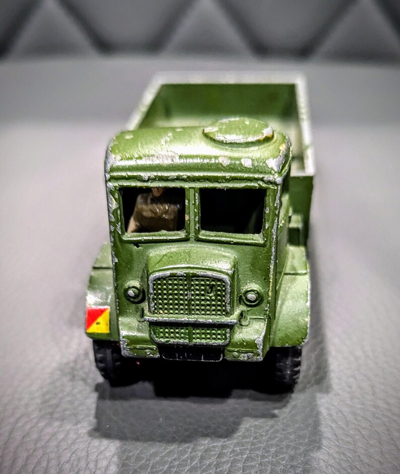 Puede incluir: Un cami&oacute;n de juguete verde con un conductor en la cabina. El cami&oacute;n tiene una plataforma y una marca amarilla y roja en el lateral.