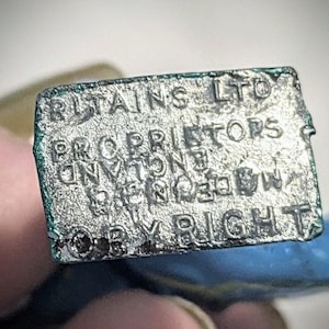 Puede incluir: Primer plano de una etiqueta de metal plateado con el texto "Britains LTD Proprietors of the "Britains" Registered Trade Mark Copyright".