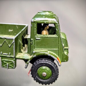 Puede incluir: Un cami&oacute;n de juguete verde con una figura de conductor dentro de la cabina. El cami&oacute;n tiene una plataforma y una carrocer&iacute;a de metal pintada de verde.