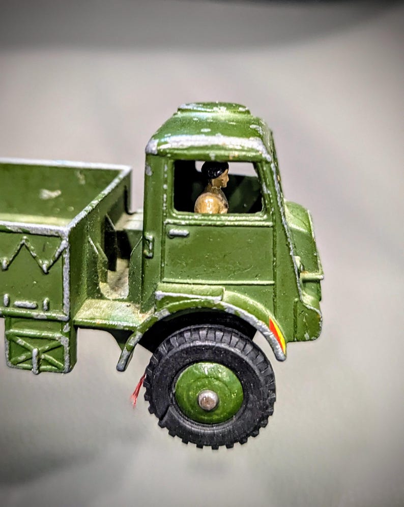 Puede incluir: Un cami&oacute;n de juguete verde con una figura de conductor dentro de la cabina. El cami&oacute;n tiene una plataforma y una carrocer&iacute;a de metal pintada de verde.