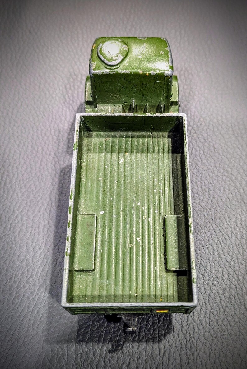 Puede incluir: Un cami&oacute;n de juguete verde con una plataforma. El cami&oacute;n es de metal y tiene un aspecto desgastado y envejecido. La plataforma est&aacute; vac&iacute;a.