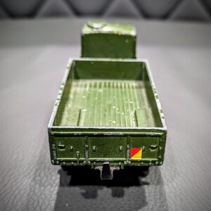 Puede incluir: Un cami&oacute;n de juguete verde con una plataforma y una bandera amarilla y roja en la parte trasera.