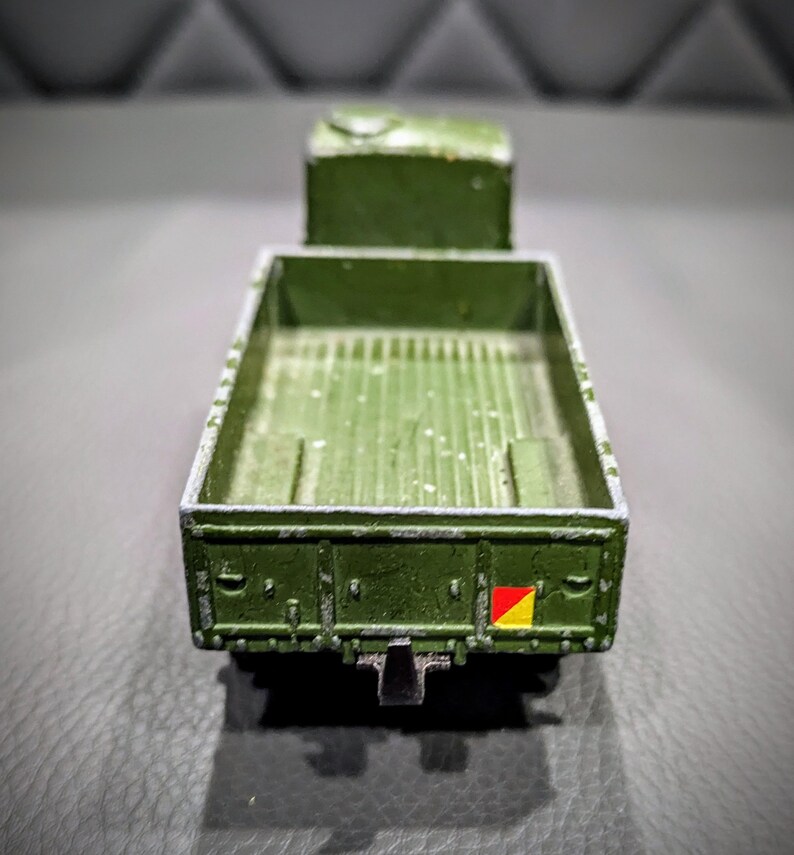 Puede incluir: Un cami&oacute;n de juguete verde con una plataforma y una bandera amarilla y roja en la parte trasera.