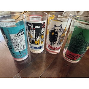 May include: Four vintage drinking glasses with gold rims, each featuring a different country's landmark. The glasses are labeled "France", "Germany", "England", and "Italy". The glasses are clear with colorful illustrations.